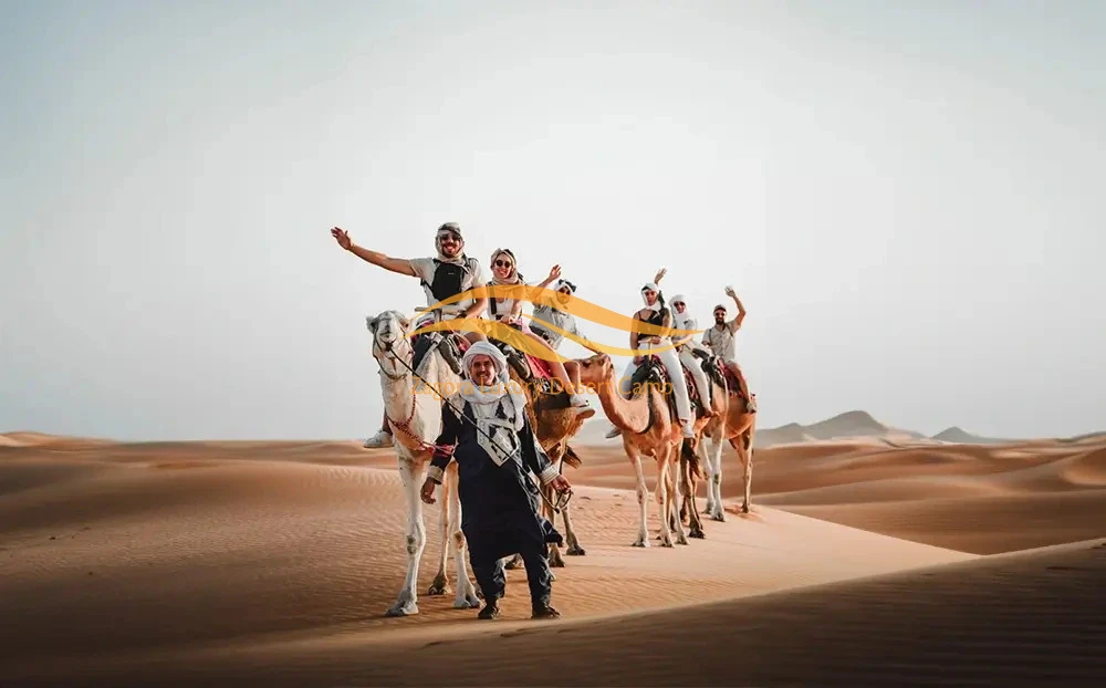 Group of travelers riding camels across the Merzouga desert dunes in Morocco